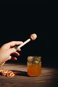 jar of honey with bagels on wooden table close up with honey dipper on black background