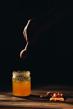 jar of honey with bagels on wooden table close up with honey dipper on black background