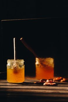 jar of honey with bagels on wooden table close up with honey dipper on black background