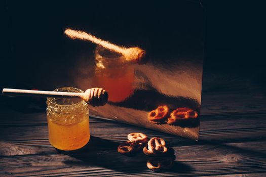 jar of honey with bagels on wooden table close up with honey dipper on black background