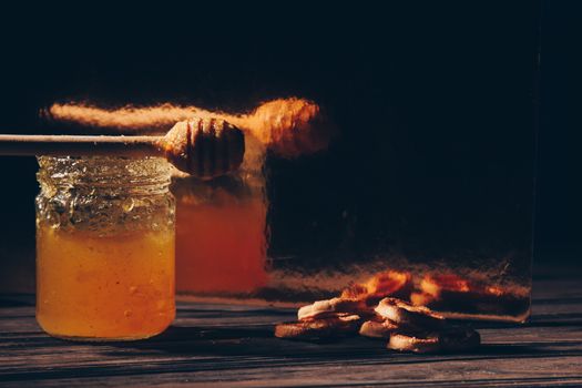 jar of honey with bagels on wooden table close up with honey dipper on black background