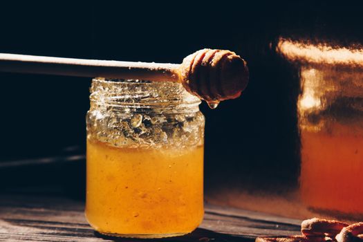 jar of honey with bagels on wooden table close up with honey dipper on black background