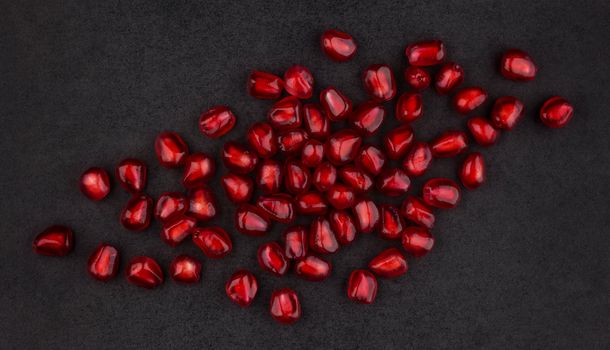 Pomegranate seeds on black background, top view, with empty space for text