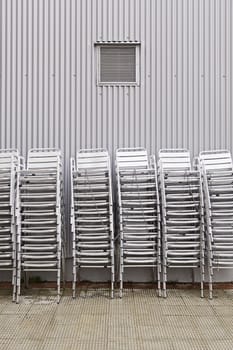 Stacked chairs on the street, detail of a mountain of chairs in the city background with metallic detail