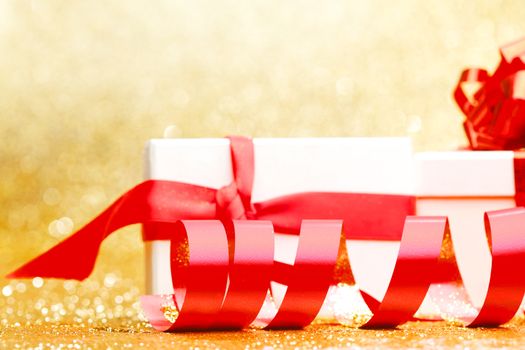 White gift box with red ribbon on golden glitter background