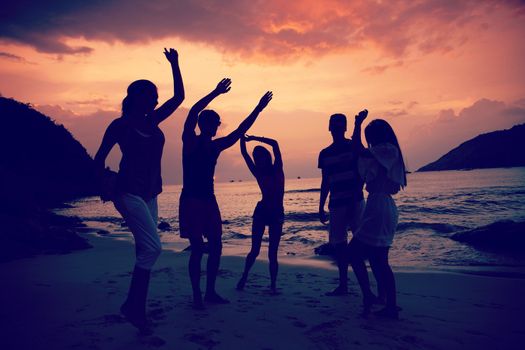 Group of happy people dancing at sea beach at sunset