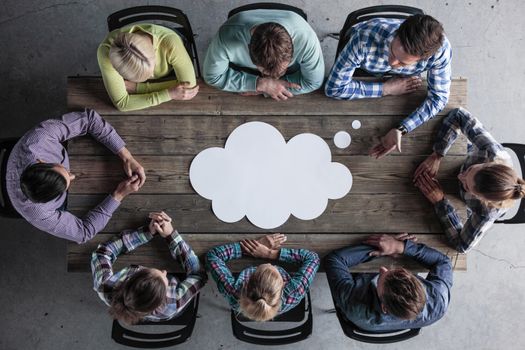 Hipster business teamwork brainstorming planning meeting concept, man tells his opinion, people sitting around the table with white paper shaped like dialog cloud