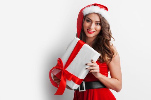 Beautiful young woman in Santa dress and hat celebrating Christmas holding gift box