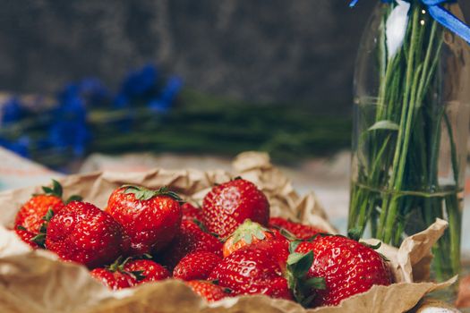 Seasonal summer flowers in vase blue cornflowers and fruits strawberries on a napkin close-up conceptual background