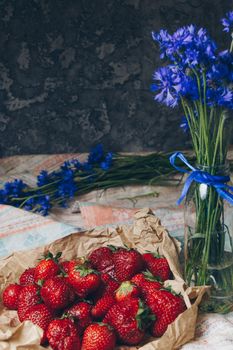 Seasonal summer flowers in vase blue cornflowers and fruits strawberries on a napkin close-up conceptual background