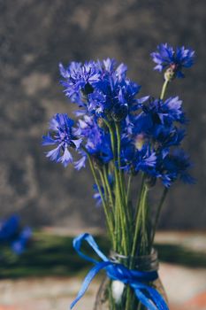 Seasonal summer flowers in vase blue cornflowers and fruits strawberries on a napkin close-up conceptual background