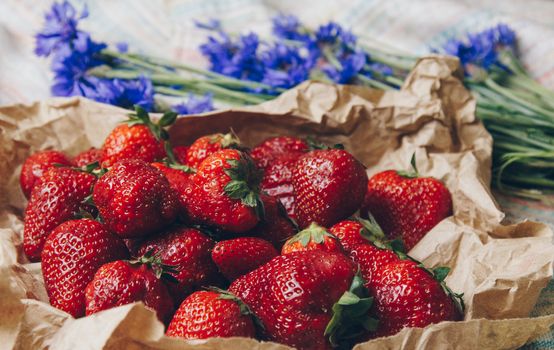 Seasonal summer flowers in vase blue cornflowers and fruits strawberries on a napkin close-up conceptual background