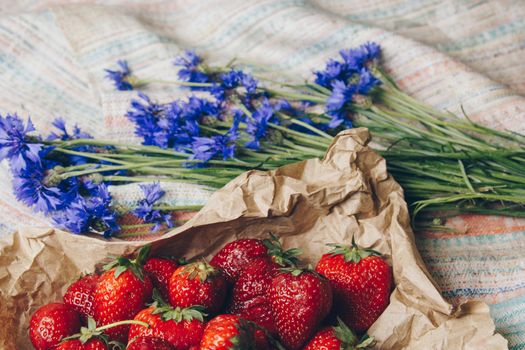 Seasonal summer flowers in vase blue cornflowers and fruits strawberries on a napkin close-up conceptual background