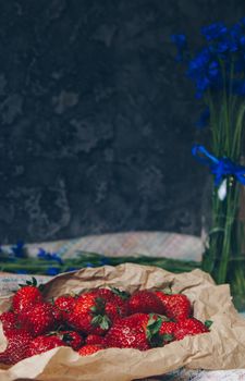 Seasonal summer flowers in vase blue cornflowers and fruits strawberries on a napkin close-up conceptual background