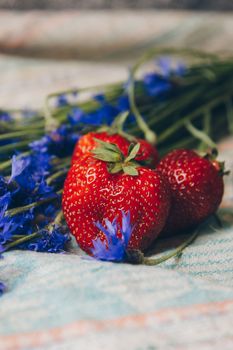 Seasonal summer flowers in vase blue cornflowers and fruits strawberries on a napkin close-up conceptual background