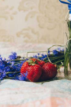 Seasonal summer flowers in vase blue cornflowers and fruits strawberries on a napkin close-up conceptual background