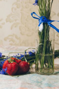 Seasonal summer flowers in vase blue cornflowers and fruits strawberries on a napkin close-up conceptual background