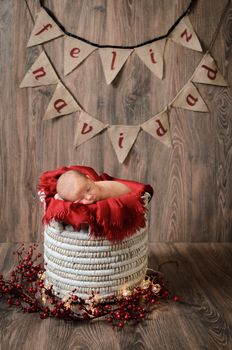 Little baby over a red blanket on a basket wishes Merry Christmas.