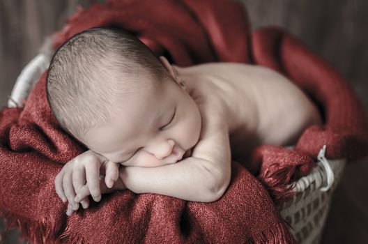 Relaxed and calm baby sleeping on a basket with a red blanket