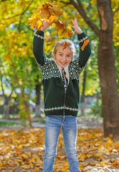 Happy girl jumping with yellow leaves in autumn