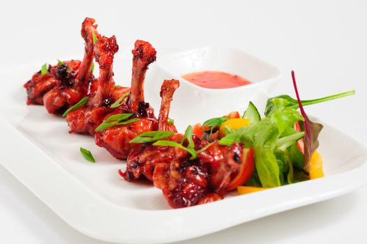 fried chicken wings fried in pomegranate sauce with vegetable salad on white plate