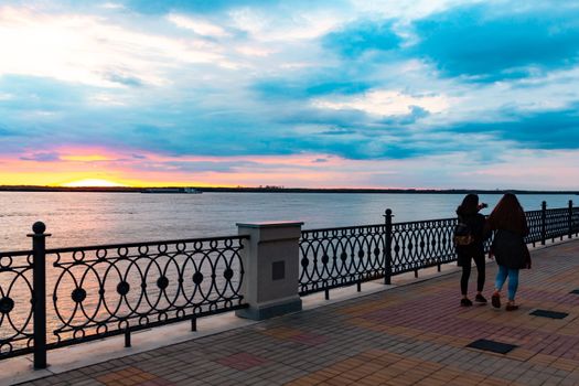 Sunset on the embankment of the Amur river in Khabarovsk. The sun set over the horizon. The embankment is lit by lanterns. People walk along the river Bank.
