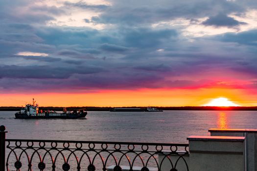 Sunset on the embankment of the Amur river in Khabarovsk. The sun set over the horizon. The embankment is lit by lanterns. People walk along the river Bank.