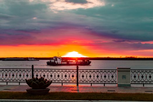 Sunset on the embankment of the Amur river in Khabarovsk. The sun set over the horizon. The embankment is lit by lanterns. People walk along the river Bank.