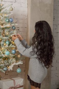 Girl decorates the Christmas tree. The view from the back.