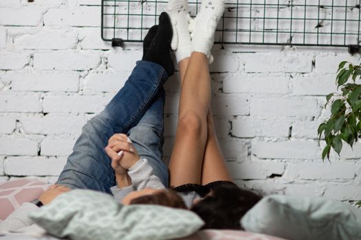 Girl and guy lay back on the bed and his feet on the wall of white brick.