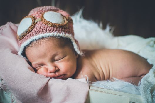 Baby sleeps peacefully in a basket wearing a funny aviator cap