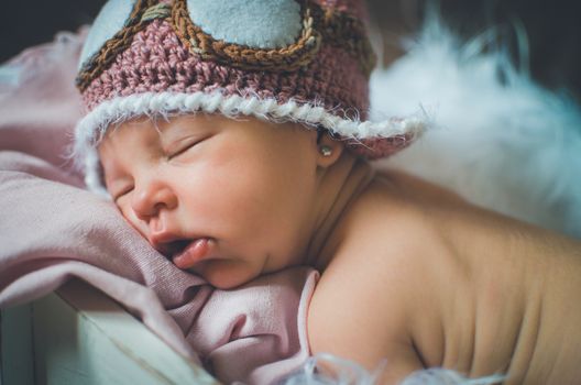 10 days old baby sleeping over a pink blanket wearing an aviator cap