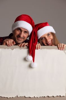 Happy couple in Santa hats holding blank banner with white copy space