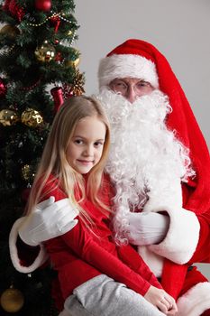 Portrait of smiling little girl sitting on santa claus knees