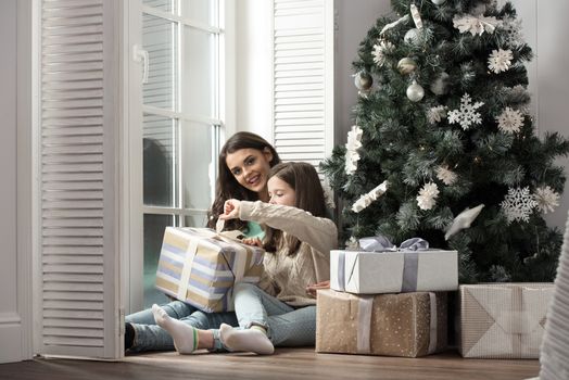 Mother and daughter unwrapping a gift sitting on the floor near christmas tree