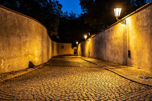 Narrow cobbled street illuminated by street lamps of Old Town, Prague, Czech Republic.