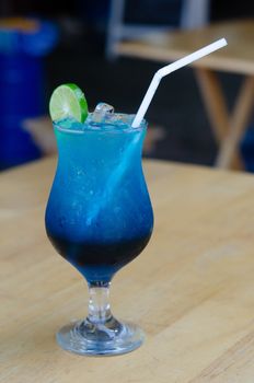 A glass of blue italian soda topped with lime on wooden table in coffee shop cafe