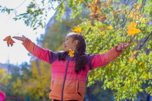 Happy girl playing with autumn yellow leaves