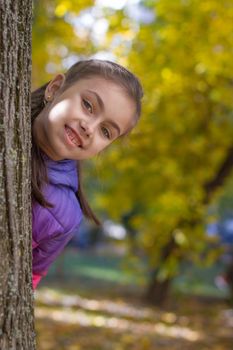 Smiling girl looking out tree in autumn park