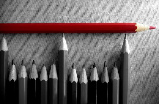 Red pencil on top of a group of pencils in black and white