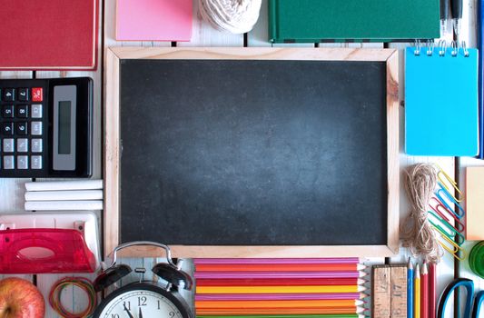 Top view of various stationery objects with blackboard in the centre