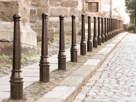 Row of iron pillars between cobbled street and pedestrian sidewalks.