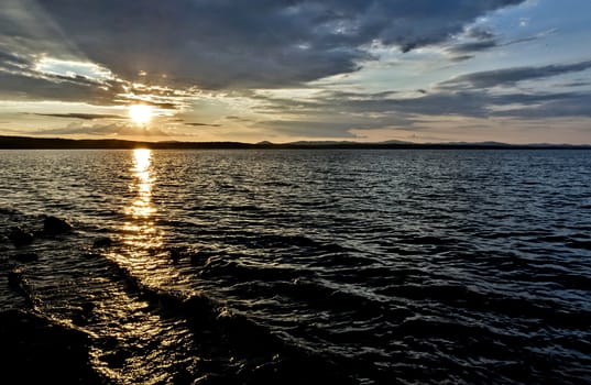 Golden sun sinks over the lake in the evening, golden water, South Ural lake Uvildy