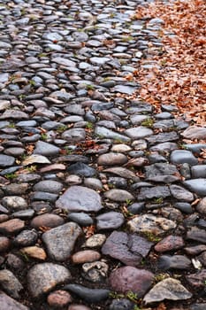 Autumn background. Old empty cobblestone roadway with leaves in provincial town