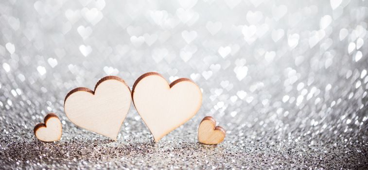 Four wooden hearts on silver glowing bokeh hearts background for Valentines day