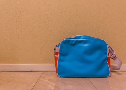 blue with red messenger school bag isolated in against a wall and standing on the floor in a room