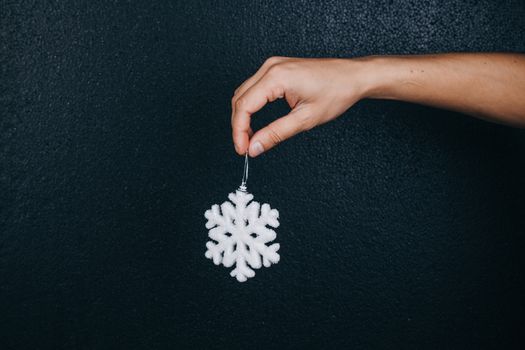 woman hand holding hanging snowflake toy for christmas decoration isolated on black background. new year gift card.