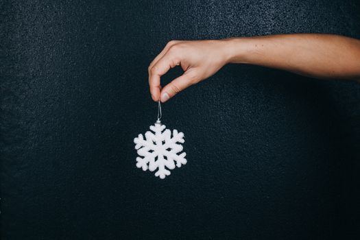 woman hand holding hanging snowflake toy for christmas decoration isolated on black background. new year gift card.