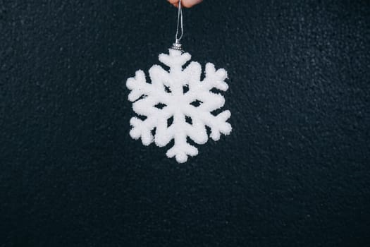 woman hand holding hanging snowflake toy for christmas decoration isolated on black background. new year gift card.