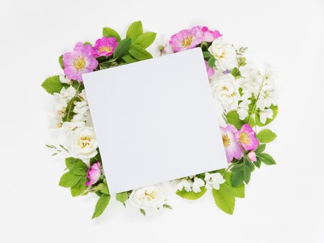 Scrapbook page of wedding or family photo album, frame with wild rose, white flowers and green leaves on light wooden background; top view, flat lay, overhead view, mocap